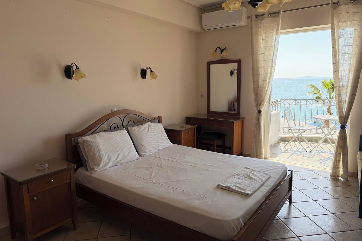 A bedroom with a bed, nightstand, dresser, and a balcony with a view of the sea.