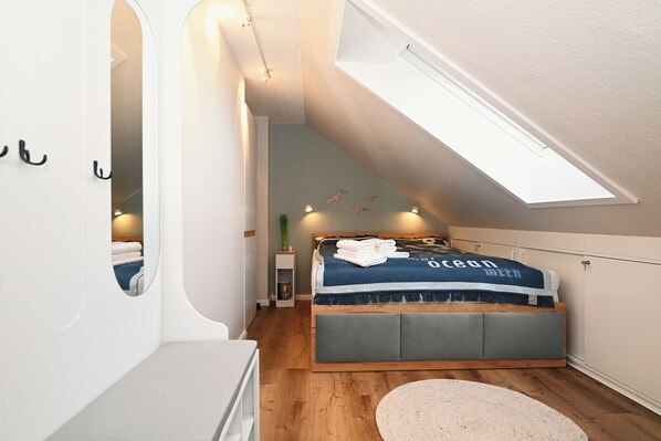 A bedroom with a skylight, a bed with a blue and white duvet, a bedside table, and a small rug. - Hus Willem - Kuschelkoje Vacation Apartment (Büsum)