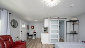 A compact room with a red leather sofa, a bed, a small kitchenette, and a walk-in closet. - Tiny House: 1BR w/ KING Bed, Pool by Raymond James (Tampa)