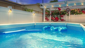 A swimming pool with a tiled edge, surrounded by a white fence and a pergola with lights. - Tiny House: 1BR w/ KING Bed, Pool by Raymond James (Tampa)