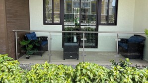 Un balcone con ringhiere in vetro, mobili in vimini e piante in vaso.