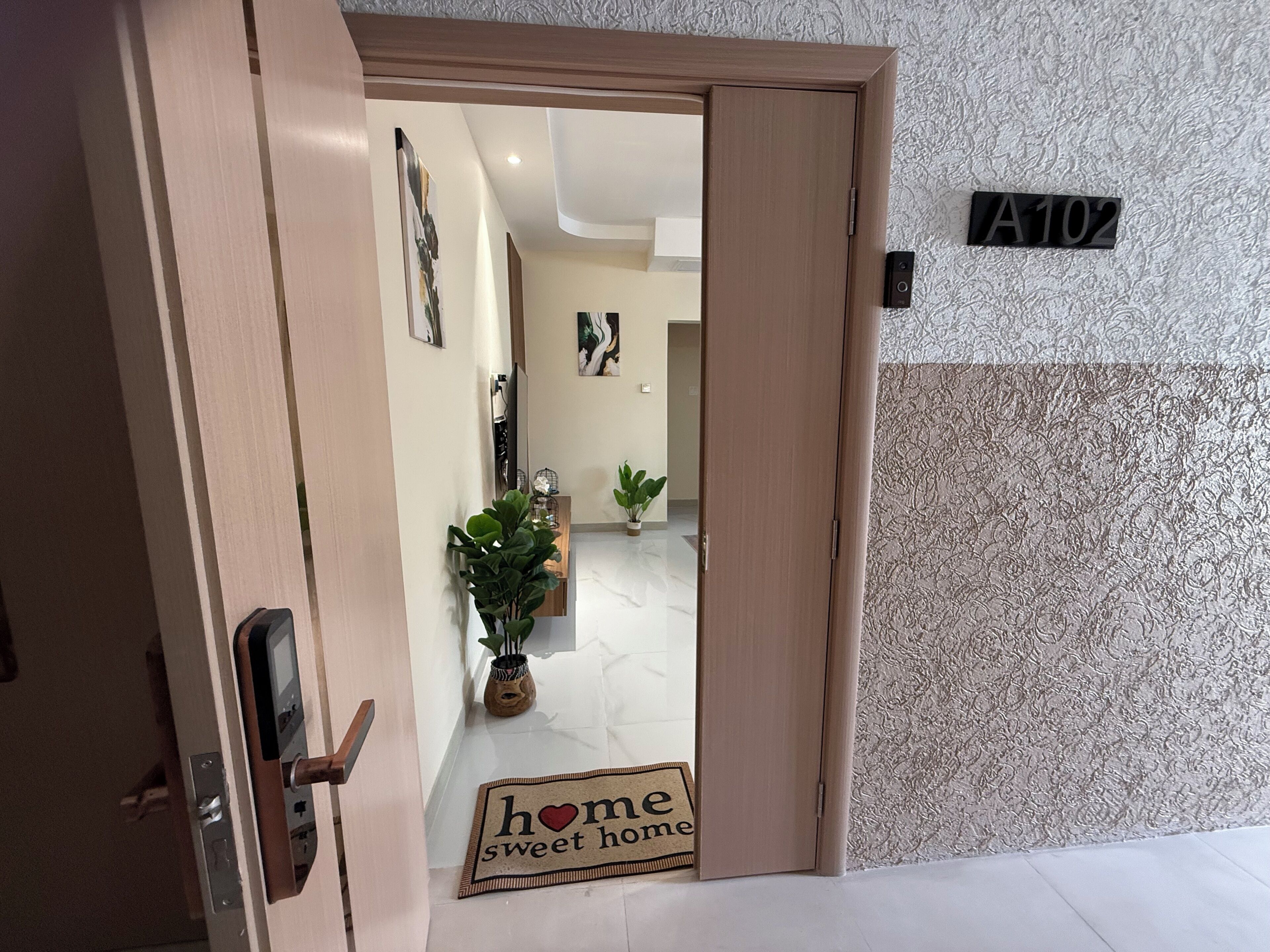 A hotel entrance with a wooden door, a welcome mat, a potted plant, and a wall-mounted sign reading "A102".