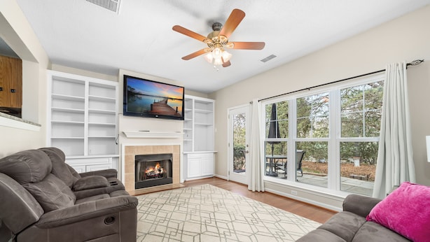A living room with a fireplace, a ceiling fan, and a large window with a view of the outdoors. - Tuscany Lane Townhouse - 2 floors, Near Lake, Pool, Pets OK - LKN Location (Cornelius)