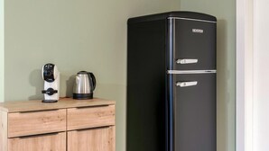 Ein schwarzer Kühlschrank der Marke SEVERIN steht neben einem Holzschrank mit Kaffeemaschine und Wasserkocher.