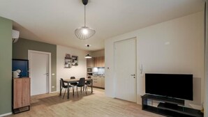 Ein modernes Wohnzimmer mit Flachbildfernseher, Essbereich und Küche im Hintergrund.