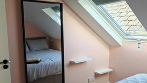 Un dormitorio con techo inclinado, tragaluz, cama, mesita de noche y espejo.