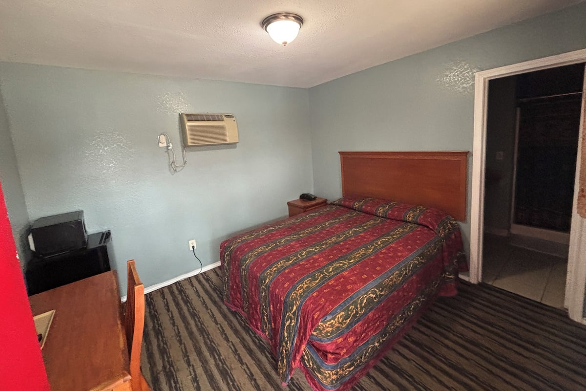 A hotel room with a bed, a desk, an air conditioning unit, and a door leading to a balcony.