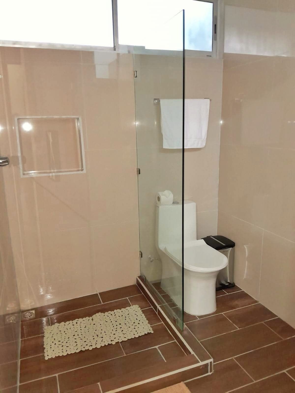 Une salle de bain avec une douche à parois de verre, des toilettes et une petite poubelle.