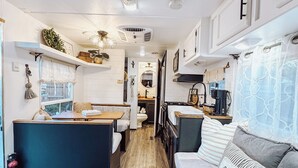 Ein kompaktes Wohnmobil-Interieur mit Küchenzeile, Essbereich und Wohnbereich inklusive Sofa und Kissen mit dem Aufdruck 'Familie'.