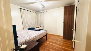 Une chambre avec un lit, un bureau, une chaise, un ventilateur de plafond et une porte.