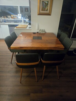 Un tavolo da pranzo in legno con quattro sedie, un piccolo dispositivo elettronico nero sul tavolo e una finestra che si affaccia su un angolo cottura.