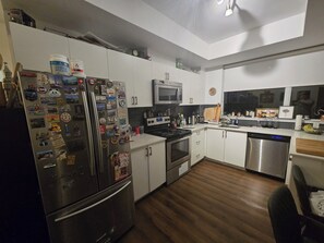 A modern kitchen with white cabinets, stainless steel appliances, and wooden flooring.