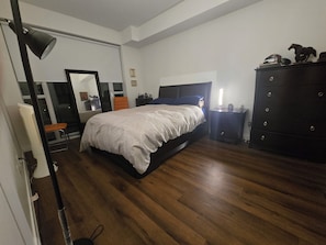 A bedroom with a large bed, a dresser, a nightstand, a chair, and a desk.