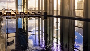 Una amplia piscina interior con techo de cristal que refleja el cielo y las nubes.