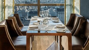 Comedor con una mesa dispuesta para cuatro, amplias ventanas que ofrecen vista a la ciudad y una lámpara colgante moderna sobre la mesa.