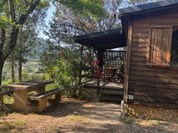 Una cabaña rústica de madera con un porche, rodeada de árboles y una mesa de picnic.