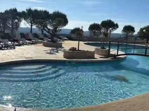 Zona de piscina con sillones de descanso y macetas, rodeada de árboles y un cielo despejado.