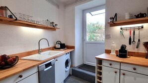 A compact kitchen with a dishwasher, washing machine, wooden countertops, and built-in shelves. - Cozy village house - 4 guests (Bellegarde-en-Forez)