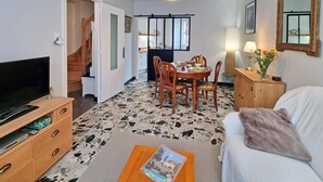 A living room with a TV, wooden furniture, a dining area, and a staircase leading to another room. - Cozy village house - 4 guests (Bellegarde-en-Forez)