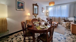 A hotel room with a dining area, a sofa, a TV, and a large window with curtains. - Cozy village house - 4 guests (Bellegarde-en-Forez)