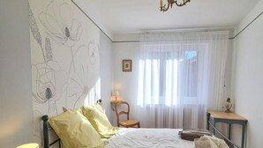 A bedroom with a bed, a nightstand, a chair, a table, and a chandelier. - Cozy village house - 4 guests (Bellegarde-en-Forez)
