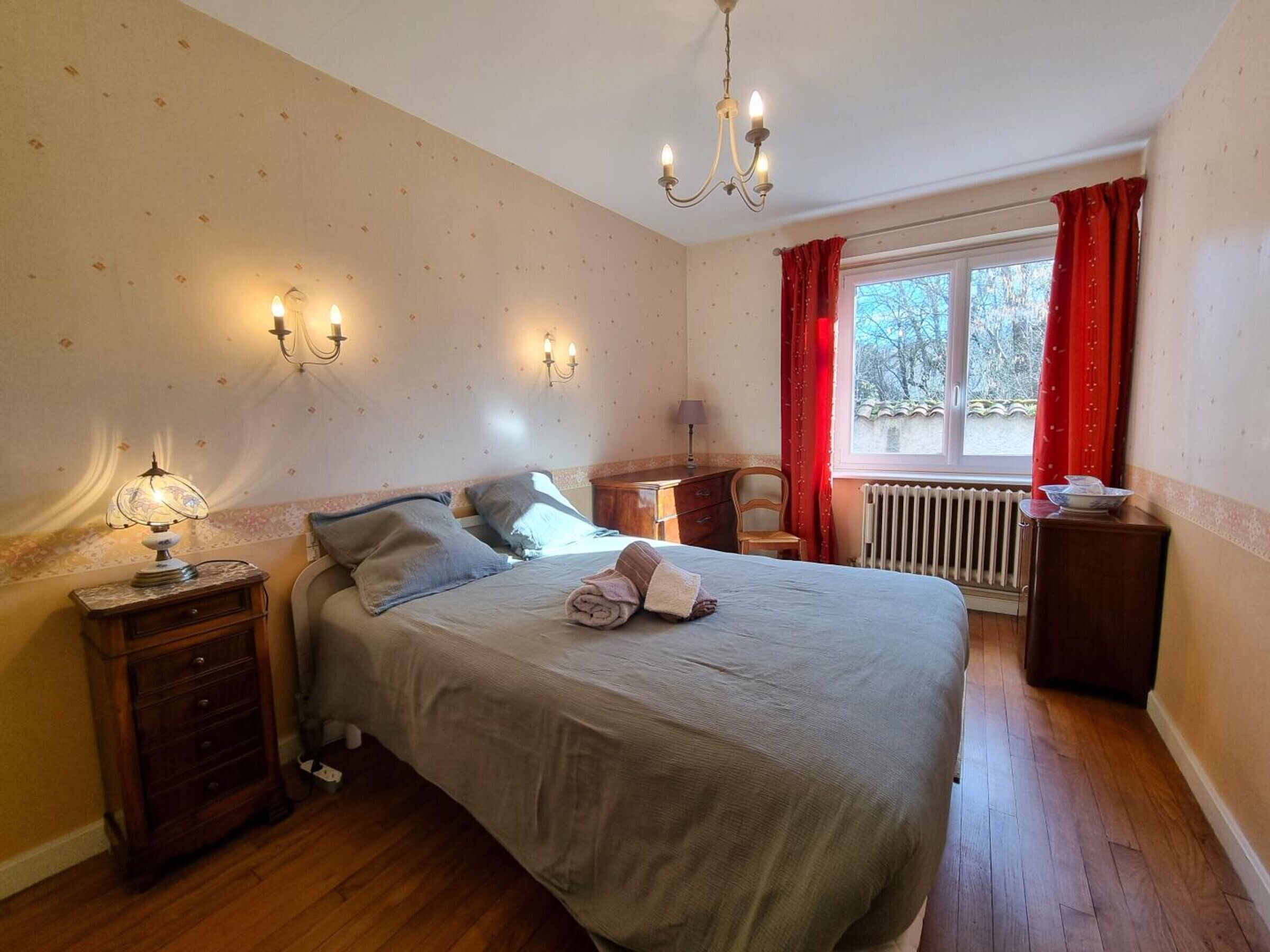 A bedroom with a bed, nightstands, a dresser, a window with curtains, and a radiator.