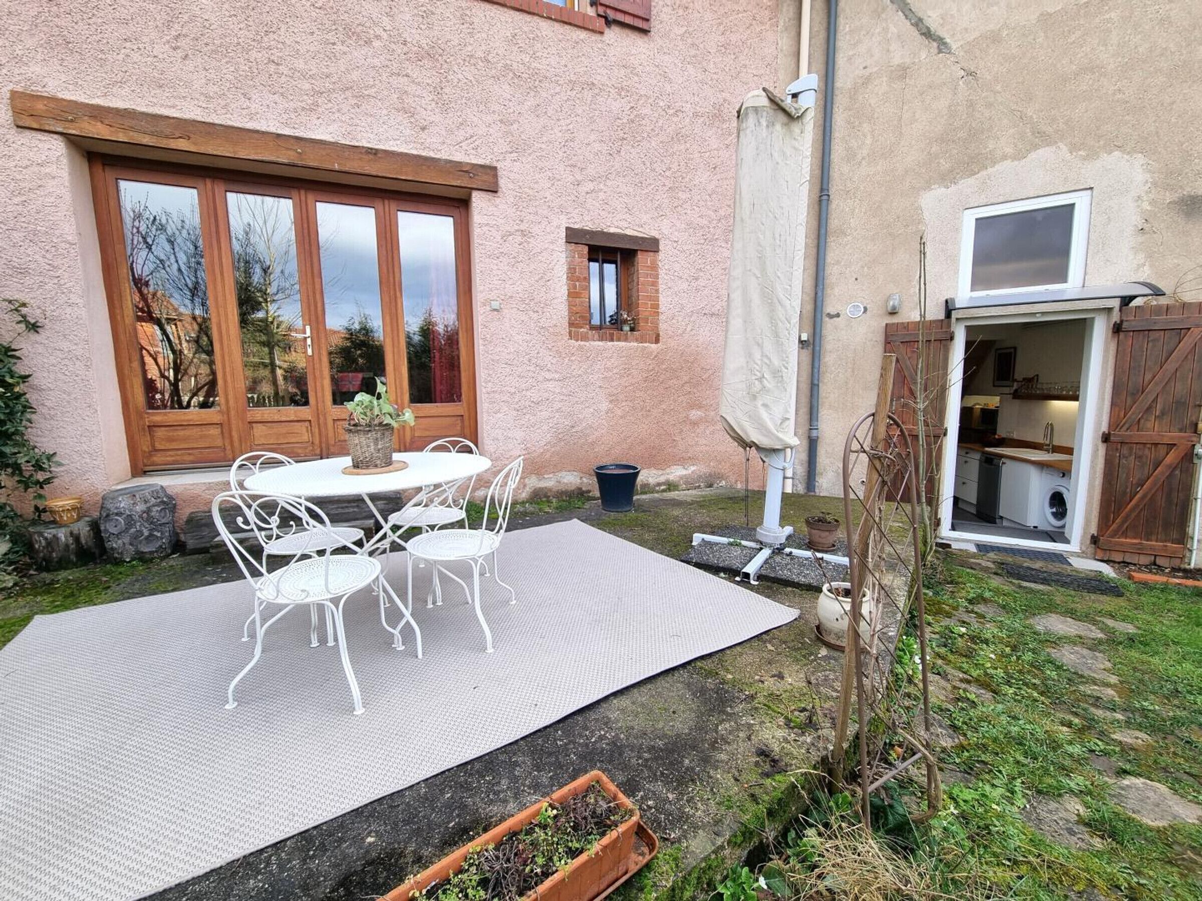 Un patio con mesa y sillas, un pequeño jardín y una puerta de madera que da a una cocina.