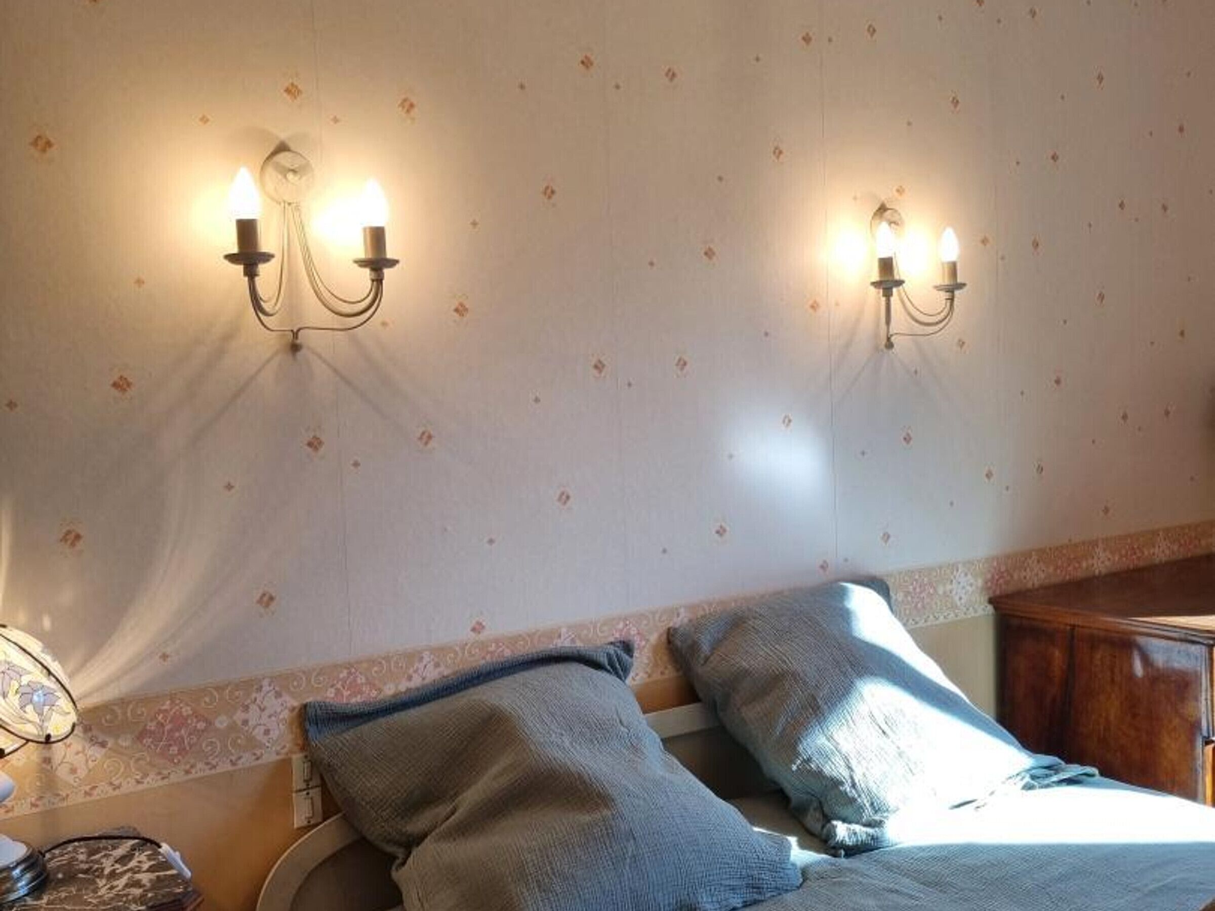 Una habitación de hotel con una cama, dos lámparas adosadas a la pared y un papel tapiz estampado.