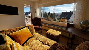 A cozy living room with a sofa, armchair, and ottoman, a table with a globe, and a large window offering a view of the outdoors. - Panorama Joy #1 (EG) (Schmallenberg)