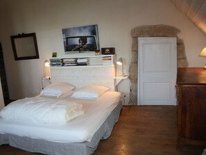 Une chambre à coucher comprenant un lit, une table de chevet, un téléviseur fixé au mur, une porte et une armoire en bois.