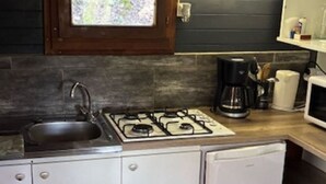 Una cocina compacta con estufa a gas, lavamanos y cafetera.