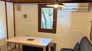 Habitación pequeña con cama, una mesita, un sofá y ventana con vista a árboles.