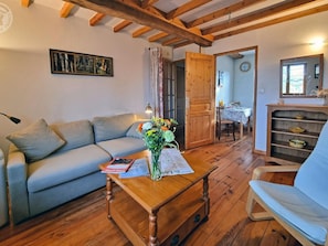 Un salon chaleureux avec un canapé, une table basse en bois ornée d’un vase de fleurs, un coin repas avec une table et des chaises, et un meuble en bois avec des étagères.