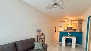 Um espaço compacto para viver, com sofá, mesa pequena, cozinha compacta e luminária no teto.