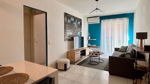 Uma sala de estar com sofá, televisão, mesinha e um espaço de refeições com cadeira e mesa.