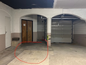 An indoor parking area with a closed garage door, a wooden door, and a concrete floor. - Apartment sea view, parking - 4 guests (Canet-en-Roussillon)