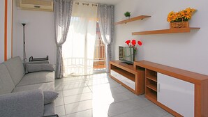 A living room with a sofa, TV, and wooden shelves with flowers. - Apartment for 4, near beach - AC (Lloret de Mar)