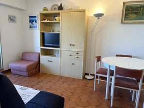 A compact living space with a sofa, a small dining table with chairs, a television on a cabinet, and a lamp. - 2-room apartment with air conditioning, sea view in Bormes-les-Mimosas (Bormes-les-Mimosas)