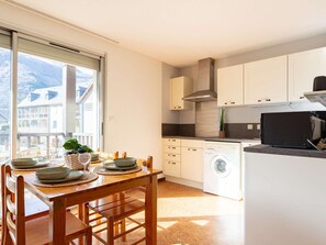 A modern kitchen with a built-in washing machine, wooden dining table, and large windows offering a view of the mountains. - Functional T3 with terrace and parking, Saint-Lary-Soulan (Saint-Lary-Soulan)