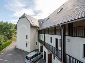 Un immeuble à la façade blanche, doté de nombreux balcons et comprenant un espace de stationnement où se trouve une voiture argentée.