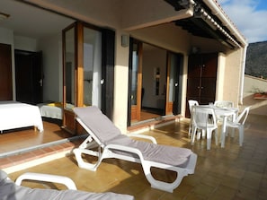 A sunlit patio with white lounge chairs and a table, a bedroom with a bed and a nightstand, and a sliding glass door leading to an outdoor area. - Apartment sea view with parking - 4 guests (Bormes-les-Mimosas)