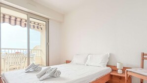 A hotel room with a bed, a wooden nightstand, a chair, and a balcony with a view. - Apartment with panoramic sea view - 4 guests (Bormes-les-Mimosas)