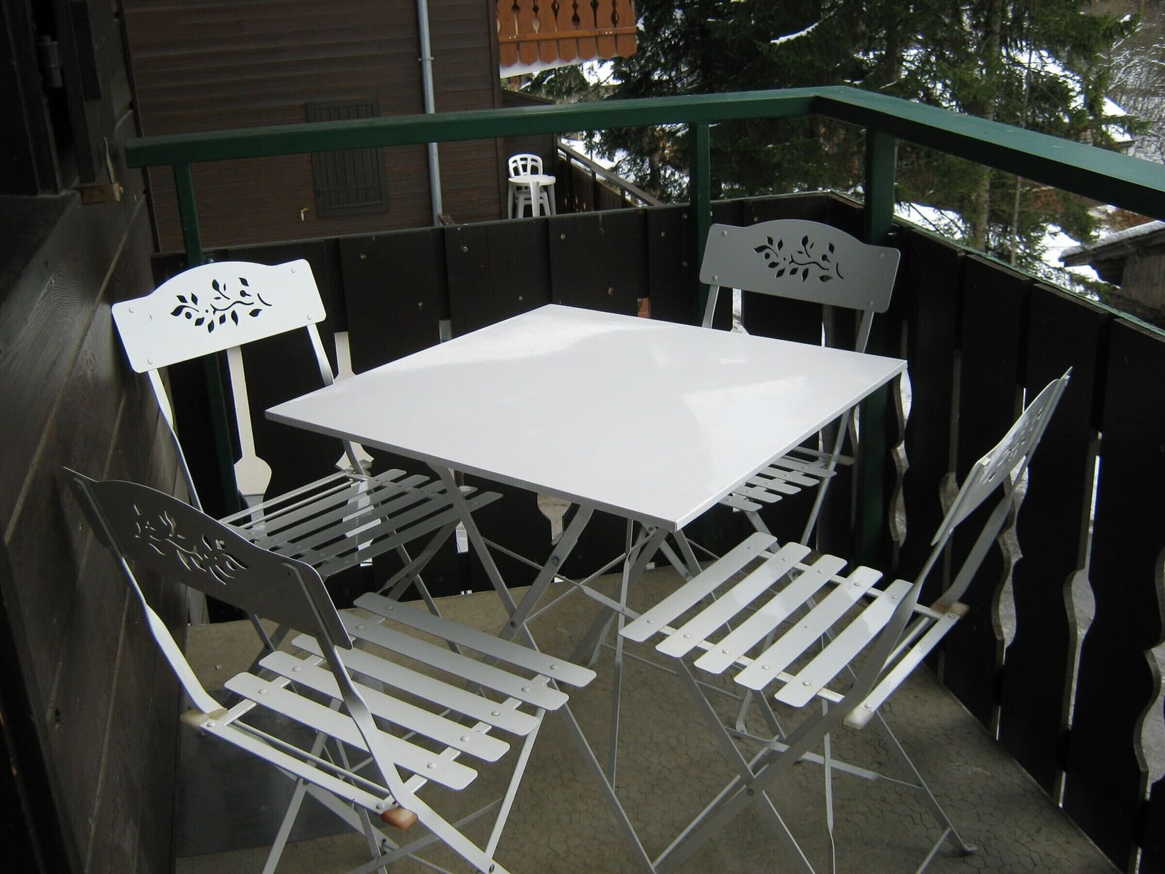 Conjunto de mesa e cadeiras brancas em varanda com guarda-corrimão de metal.
