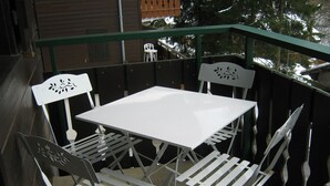 Une table et des chaises blanches sont disposées sur un balcon doté d’une rambarde en métal.
