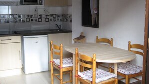 Une cuisine compacte équipée d’un four à micro-ondes, d’un évier et d’un petit réfrigérateur. On y trouve une table à manger en bois avec quatre chaises, ainsi qu’un petit meuble de rangement au-dessus de l’évier.
