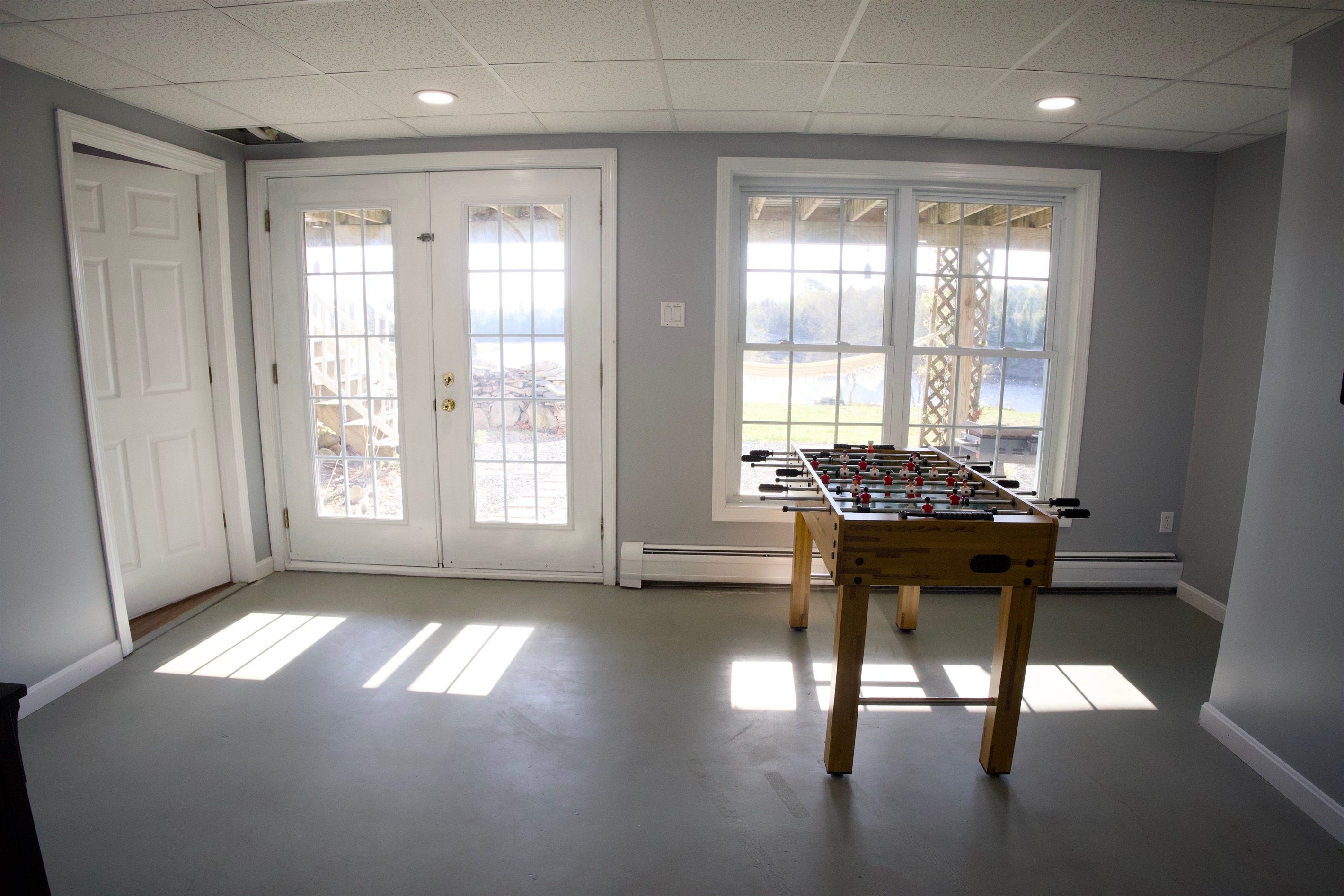 A room with a foosball table, two double doors, and large windows with a view.