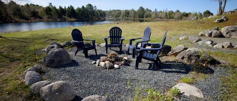 A gravel area with three Adirondack chairs, a fire pit, and a lake view.
