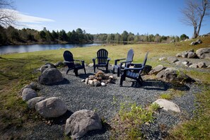 Un espace recouvert de gravier avec trois fauteuils Adirondack, un foyer et une vue sur le lac.