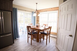 Eine Küche mit Holztisch, Stühlen, einem Kühlschrank und einem Fenster mit Vorhängen.
