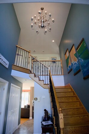 Eine Treppe mit Holzbodenstufen und schwarzen Geländern, ein Chandelier und Kunstwerke an den Wänden.